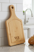 Wooden cutting board with 'VUE REALTY' branding on a kitchen counter with bread and herbs.