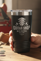 Person holding a black tumbler with 'Guitar Shop Rocking' text in a guitar shop setting
