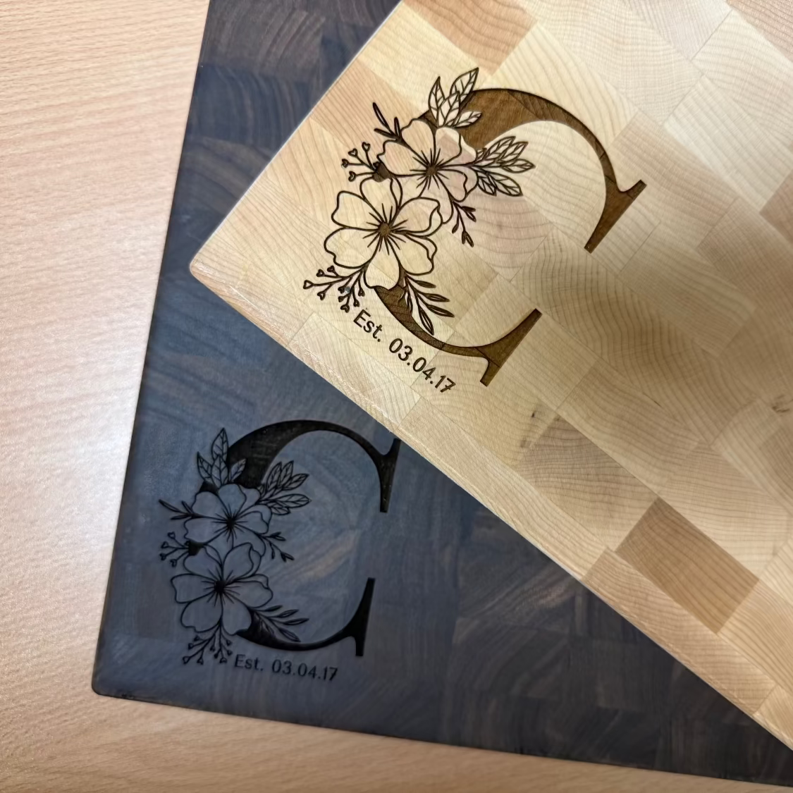 Two wooden End Grain Butcher Block Boards with floral monogram designs on a light wood surface.