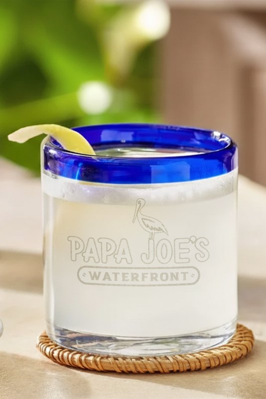 Clear glass with blue rim containing a drink, garnished with a lemon slice, on a wooden table.