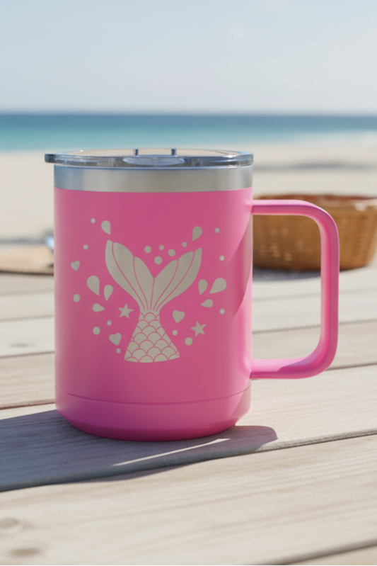 Pink mug with a mermaid design on a wooden surface at the beach